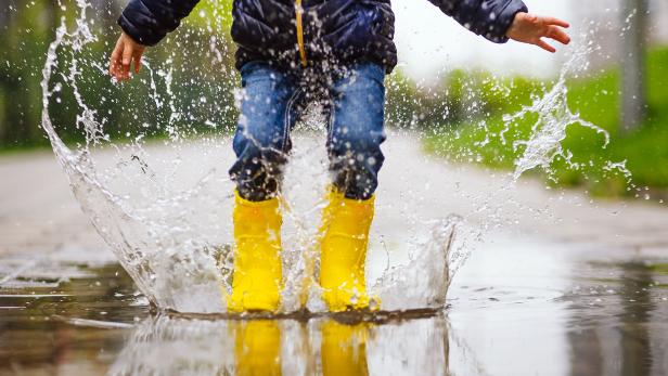 Close up legs of child with yellow rubber boots jump in puddle on an autumn walk