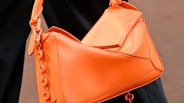 Eine Person hält eine orangefarbene Loewe Puzzle Bag mit Kettenelementen.