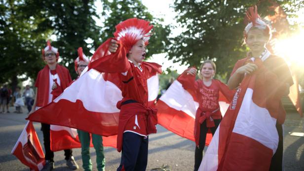 Eine Gruppe junger dänischer Fans mit rot-weißen Hüten und Flaggen jubelt.