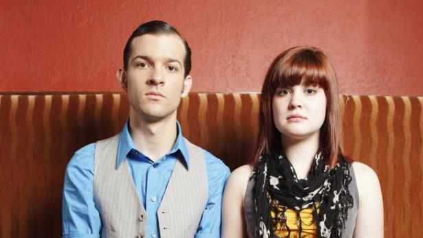 Ein Mann und eine Frau sitzen nebeneinander auf einer roten Bank.