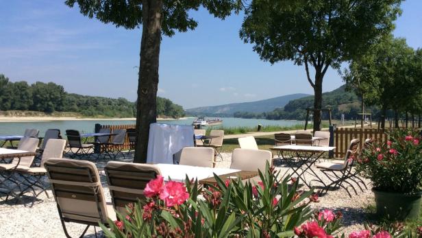 Ein Restaurantgarten mit Blick auf einen Fluss an einem sonnigen Tag.