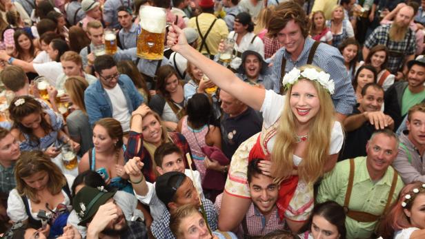 Eine Menschenmenge in Tracht feiert mit Bierkrügen auf dem Oktoberfest.