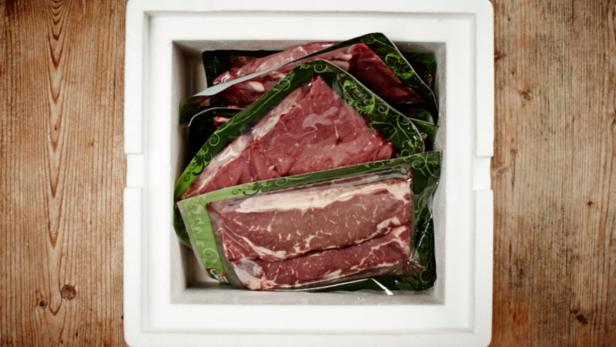 Verpacktes rohes Fleisch in einer weißen Styroporbox auf einem Holztisch.