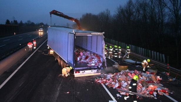 Ein umgekippter Lastwagen auf einer Autobahn wird von Feuerwehrleuten begutachtet.
