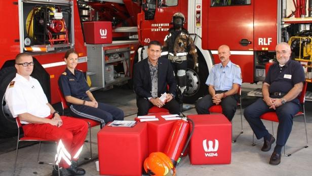 Eine Gruppe von Personen sitzt vor einem roten Feuerwehrfahrzeug für eine Präsentation.