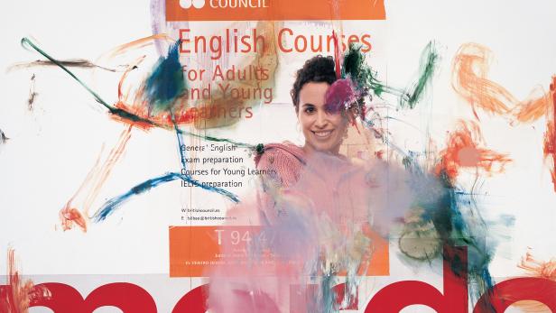 Eine Frau lächelt vor einem Werbeplakat des British Council für Englischkurse.