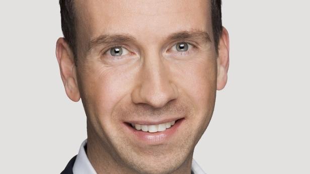 Porträt eines lächelnden Mannes mit hellen Augen vor einem neutralen Hintergrund.