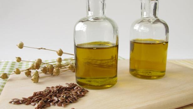 Zwei Flaschen Leinöl stehen neben Leinsamen auf einem Holzbrett.