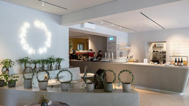 Innenansicht eines Cafés mit Pflanzen und einer leuchtenden Neonreklame.