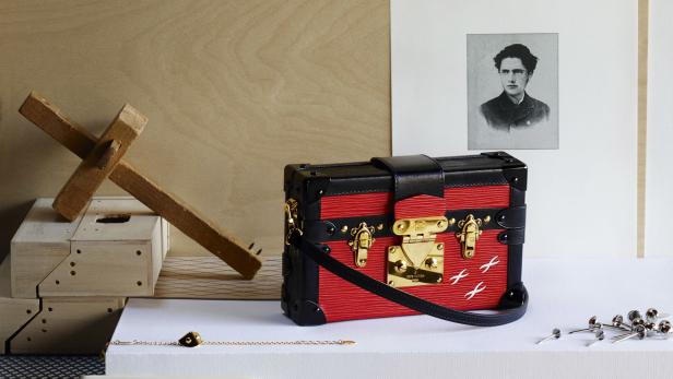 Eine rote Louis Vuitton Petite Malle Handtasche vor einem Porträt und Werkzeugen.
