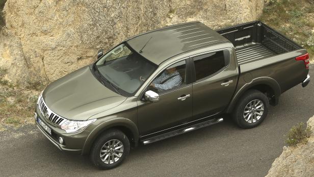 Ein olivgrüner Mitsubishi L200 Pickup fährt auf einer Straße.