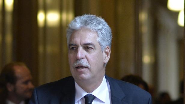 Ein Mann mit grauem Haar und Schnurrbart trägt einen dunklen Anzug.