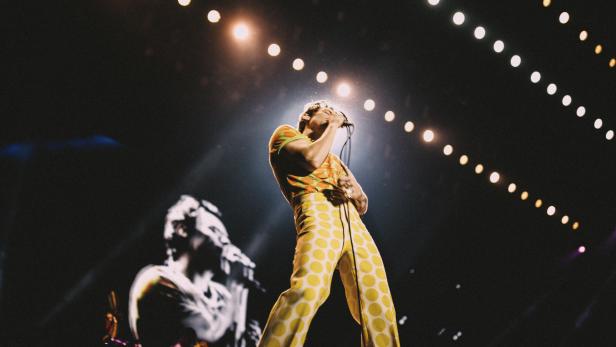 Harry Styles tritt in einem bunten Anzug auf einer Bühne auf.