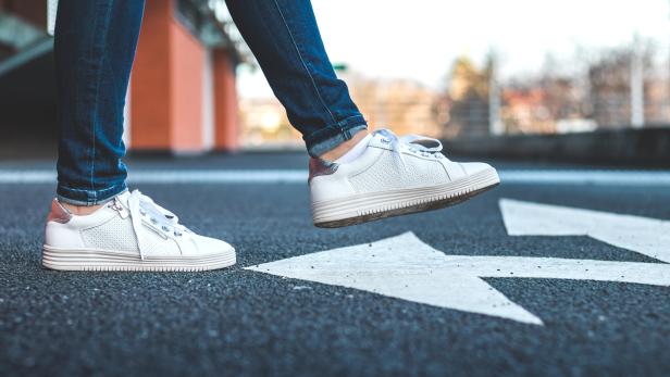 Eine Frau mit Jeans und weißen Turnschuhen geht auf einer Straße mit Richtungspfeil.