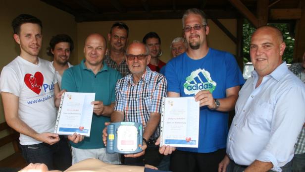 Eine Gruppe von Personen hält Urkunden und einen Defibrillator in die Kamera.
