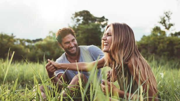 Ein Mann und eine Frau sitzen lachend in einem hohen Grasfeld.