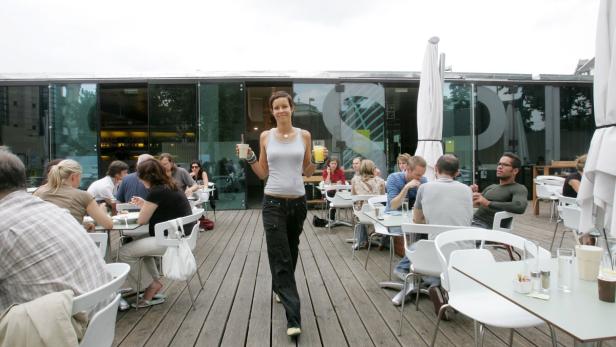Eine Kellnerin bringt Getränke auf der Terrasse eines Cafés.