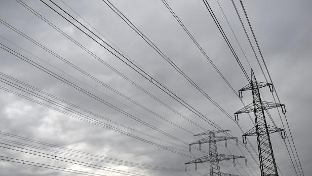 Mehrere Strommasten und Hochspannungsleitungen vor einem bewölkten Himmel.