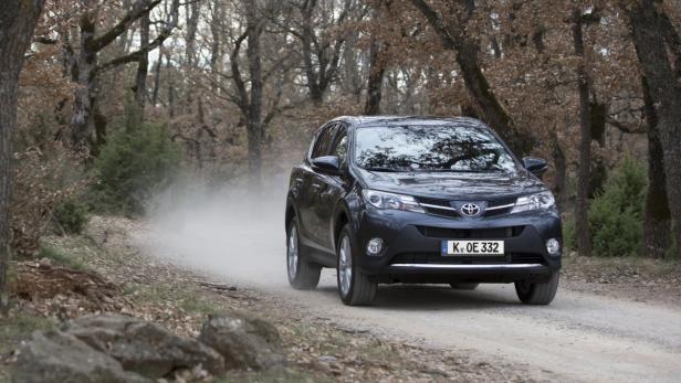 Ein grauer Toyota RAV4 fährt auf einer unbefestigten Straße durch einen Wald.