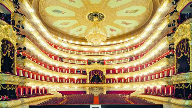 Der prunkvolle Innenraum eines Theaters mit goldenen Verzierungen und roten Sitzen.