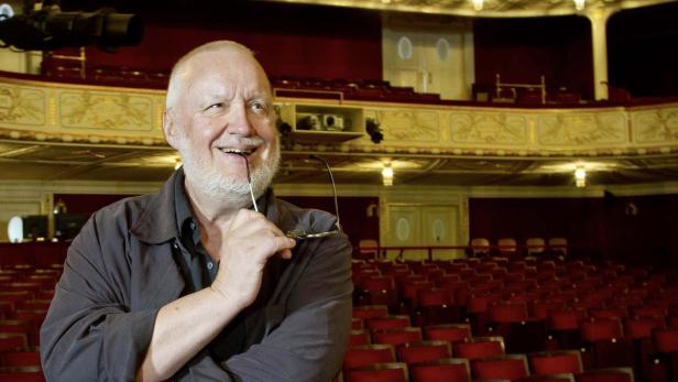 Ein Mann mit Brille im Mund steht vor einem leeren Theatersaal.