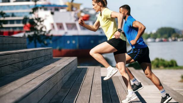 Eine Frau und ein Mann joggen eine Holztreppe hinauf.