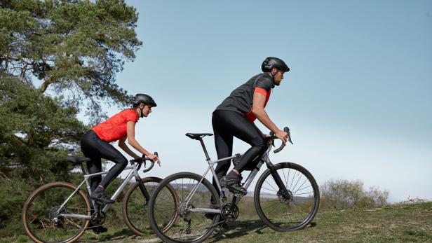 Zwei Radfahrer fahren auf ihren Fahrrädern einen grasbewachsenen Hügel hinauf.