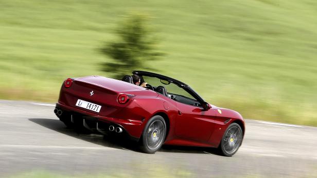 Ein roter Ferrari fährt auf einer Landstraße.