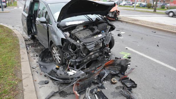Ein grauer Van mit geöffneter Motorhaube und schweren Schäden nach einem Verkehrsunfall.
