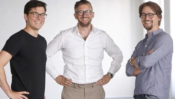 Drei Männer mit Brillen stehen lächelnd vor einem weißen Hintergrund.