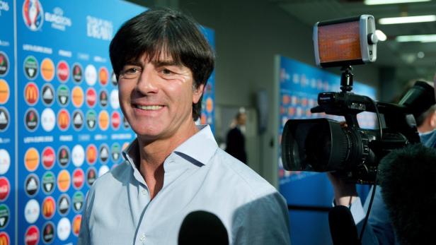 Joachim Löw lächelt vor einer Wand mit Sponsorenlogos.