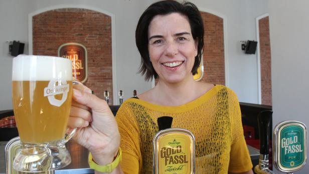 Eine Frau lächelt und hält ein Glas Ottakringer Bier in die Kamera.