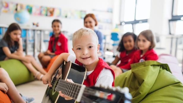 Ein Junge mit Down-Syndrom spielt Gitarre und lächelt, während andere Kinder um ihn herum auf Sitzsäcken sitzen.