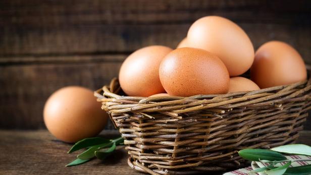 Braune Eier liegen in einem Weidenkorb auf einem Holztisch.