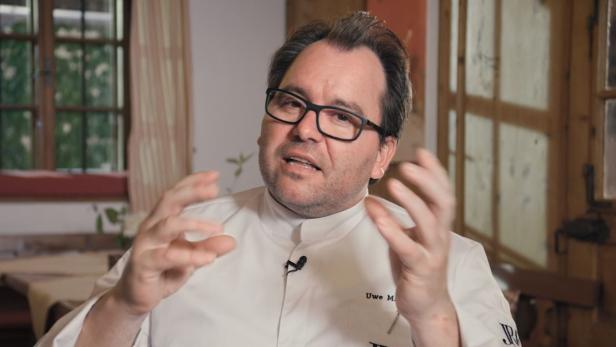 Uwe M., ein Mann mit Brille und Kochjacke, gestikuliert vor einem Fenster.