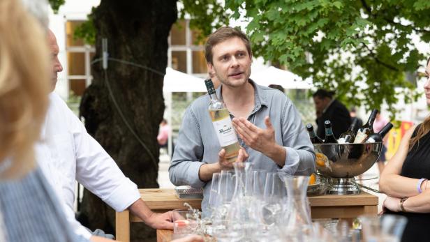 Ein Mann erklärt einer Gruppe im Freien einen Vermouth der Marke Burschik.