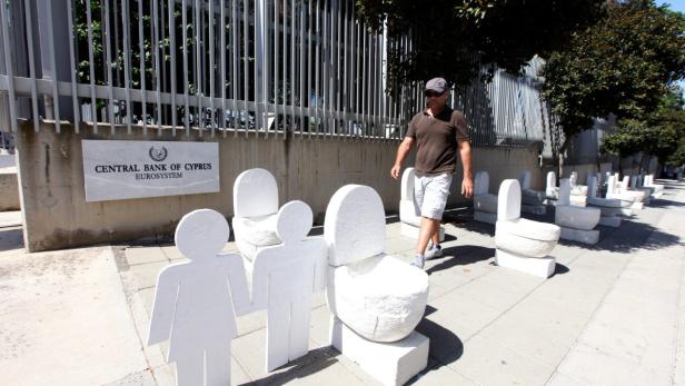 epa03738685 49-year-old painter Andreas Efstathiou stands by twenty white plaster and perlite creations that look like toilets outside the Central Bank of Cyprus building in Nicosia, Cyprus, 10 June 2013. Placed in two neat rows outside the gates of Cyprus&#039; central bank, the sculptures look like toilet bowls but also resemble tombstones - Efstathiou&#039;s vision of Cyprus&#039; tanking economy. EPA/KATIA CHRISTODOULOU