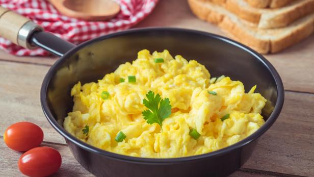 Scrambled egg in frying pan and toast on wooden table