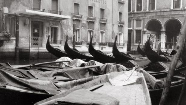 Schwarz-Weiß-Aufnahme von Gondeln, die vor dem Gebäude „Cavalletto“ in Venedig liegen.