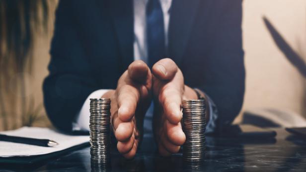 Ein Mann im Anzug trennt mit den Händen zwei Stapel Münzen auf einem Tisch voneinander.