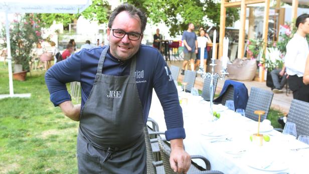 Koch Riad Machreich posiert vor einem gedeckten Tisch im Freien.