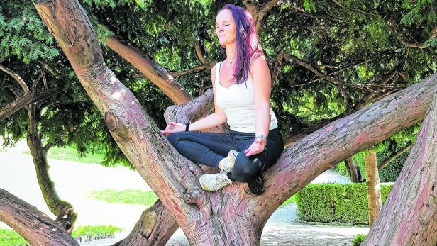 Eine Frau meditiert auf einem Ast eines Baumes in einem Park.