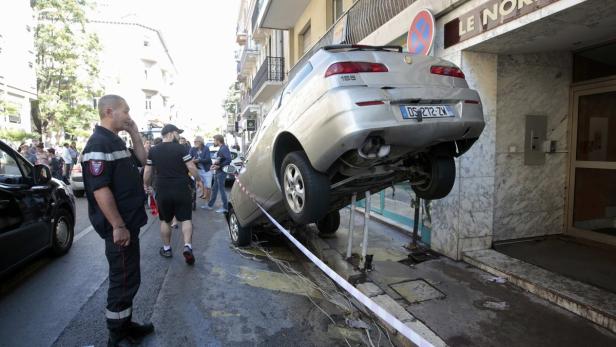 Ein Auto ist auf der Straße vor einem Gebäude auf Metallstangen aufgebockt.