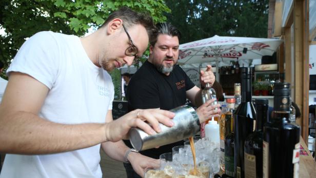 Zwei Barkeeper mixen Cocktails an einer Bar im Freien.
