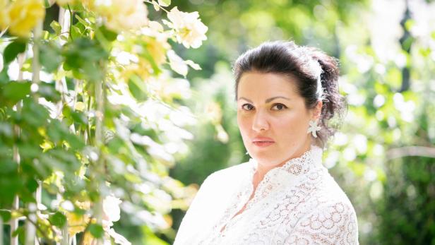 Eine Frau mit weißer Spitze steht vor gelben Rosen.