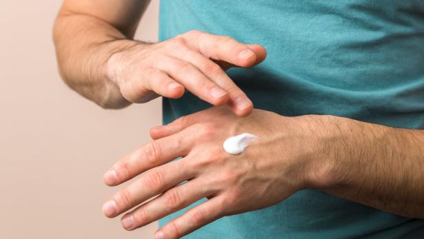 Ein Mann cremt sich die Hände ein.