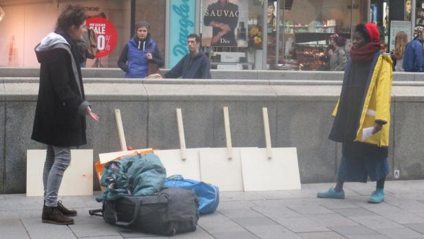 Zwei Frauen stehen vor Gepäck und leeren Schildern in einer Fußgängerzone.