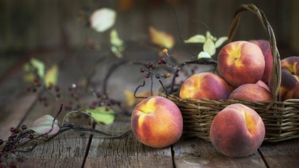 Ein Korb voller Pfirsiche auf einem rustikalen Holztisch mit herbstlicher Dekoration.