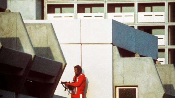 Ein Mann in roter Trainingsjacke steht mit einer Waffe auf einem Gebäude während des Olympia-Attentats.