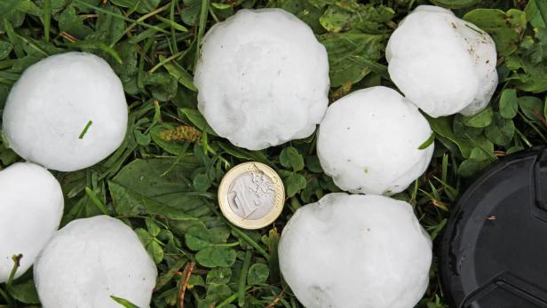 Hagelsteine liegen neben einer Ein-Euro-Münze auf einer Wiese.